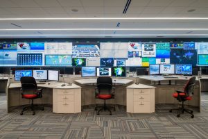 row of sit-stand consoles at different heights in front of a video wall