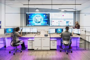 Three people working in an Operations Center with video walls and consoles
