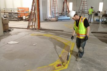 a man in a hard hat and safety vest measures a piece of wood