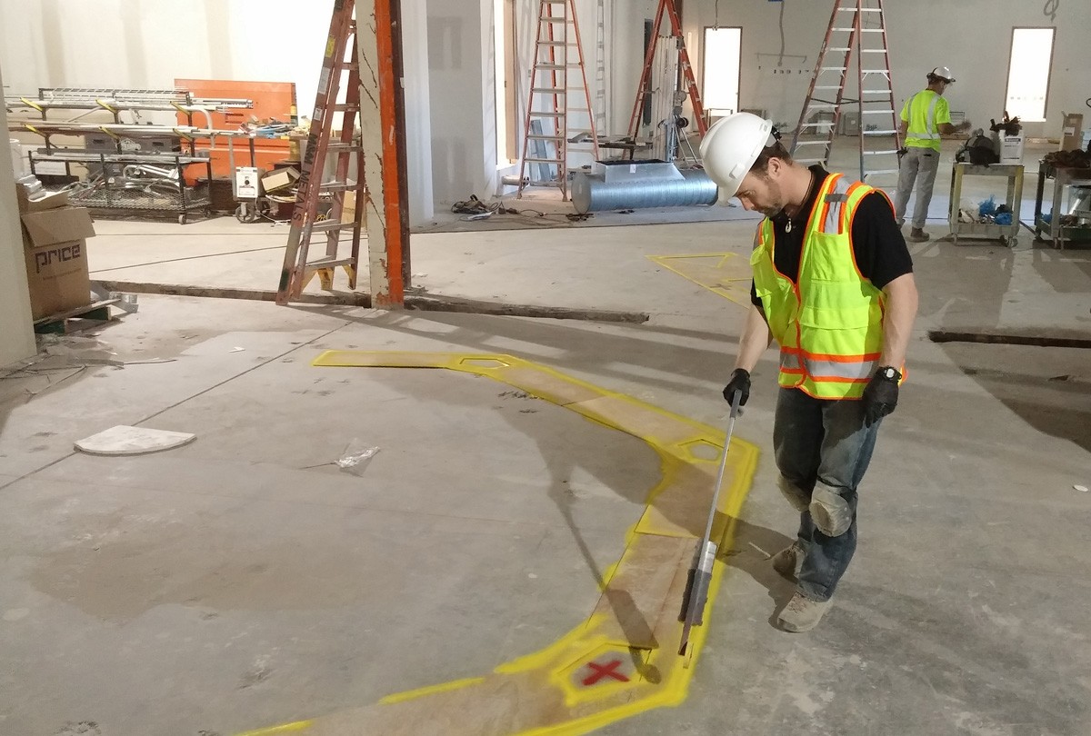 a man in a hard hat and safety vest measures a piece of wood